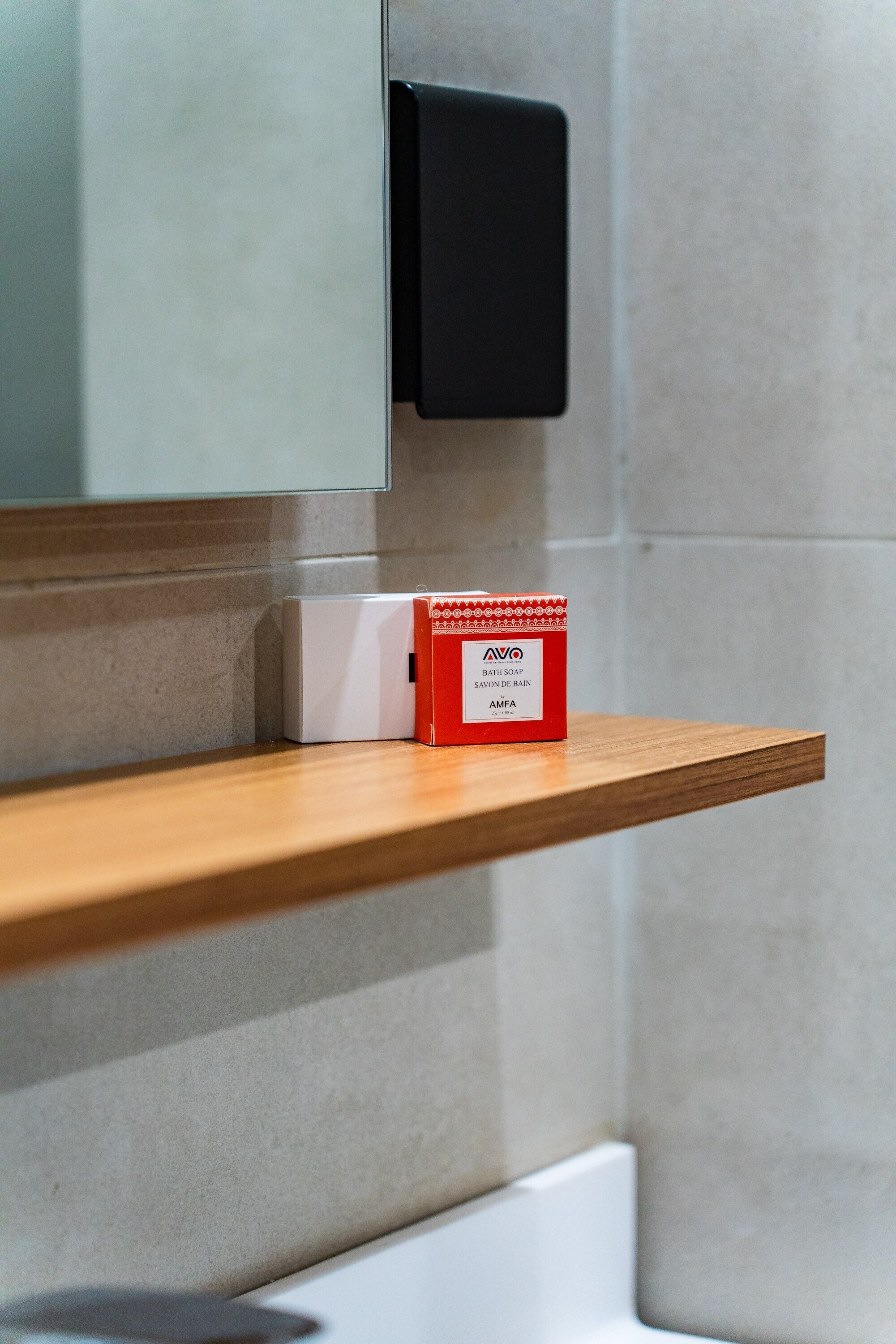 A bathroom with a wooden shelf holding a red and white bottle of AVO bath soap.