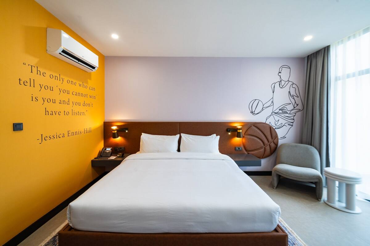 A hotel room with a large bed, a basketball-themed wall mural, and a quote by Jessica Ennis-Hill.