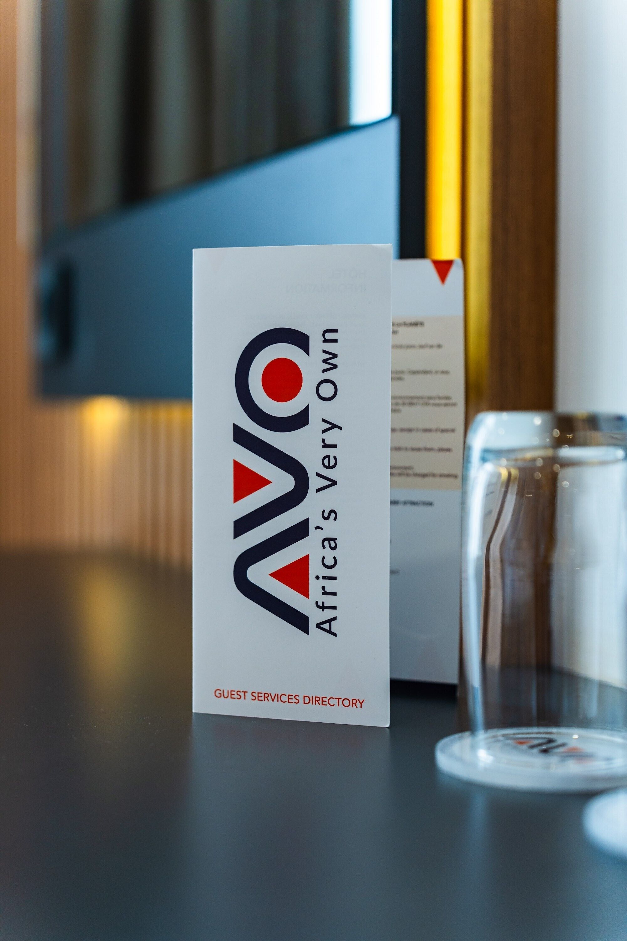 Un letrero con el texto "AVO Africa's Very Own" y "DIRECTORIO DE SERVICIOS PARA HUESPEDES" sobre una mesa.