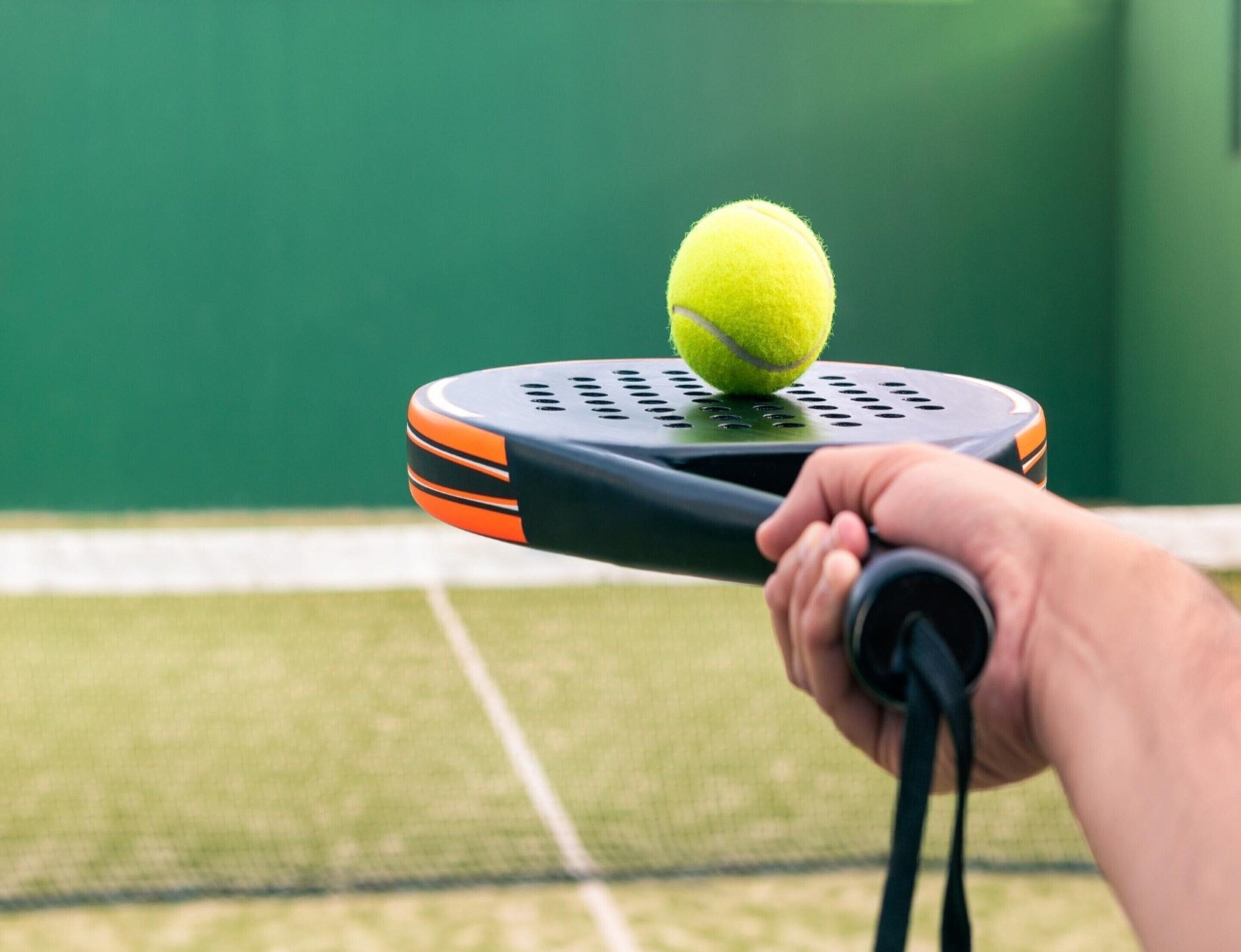 A hand holding a tennis racket with a tennis ball on it.
