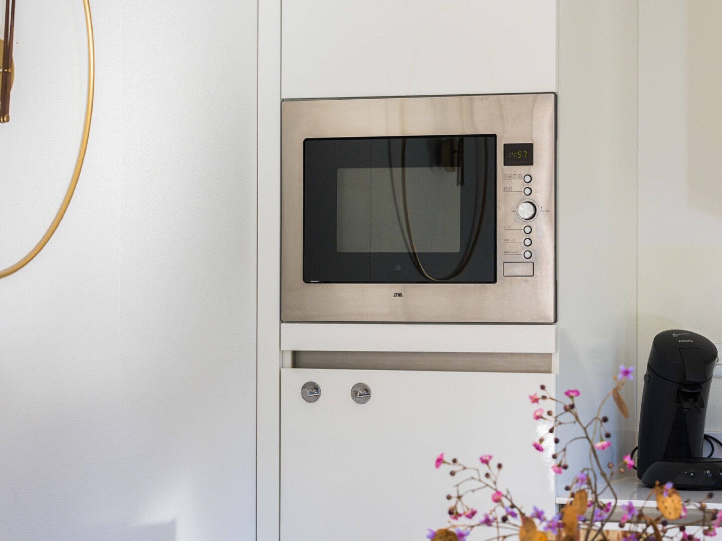 A microwave oven mounted on a white cabinet with a digital clock displaying 14:57.