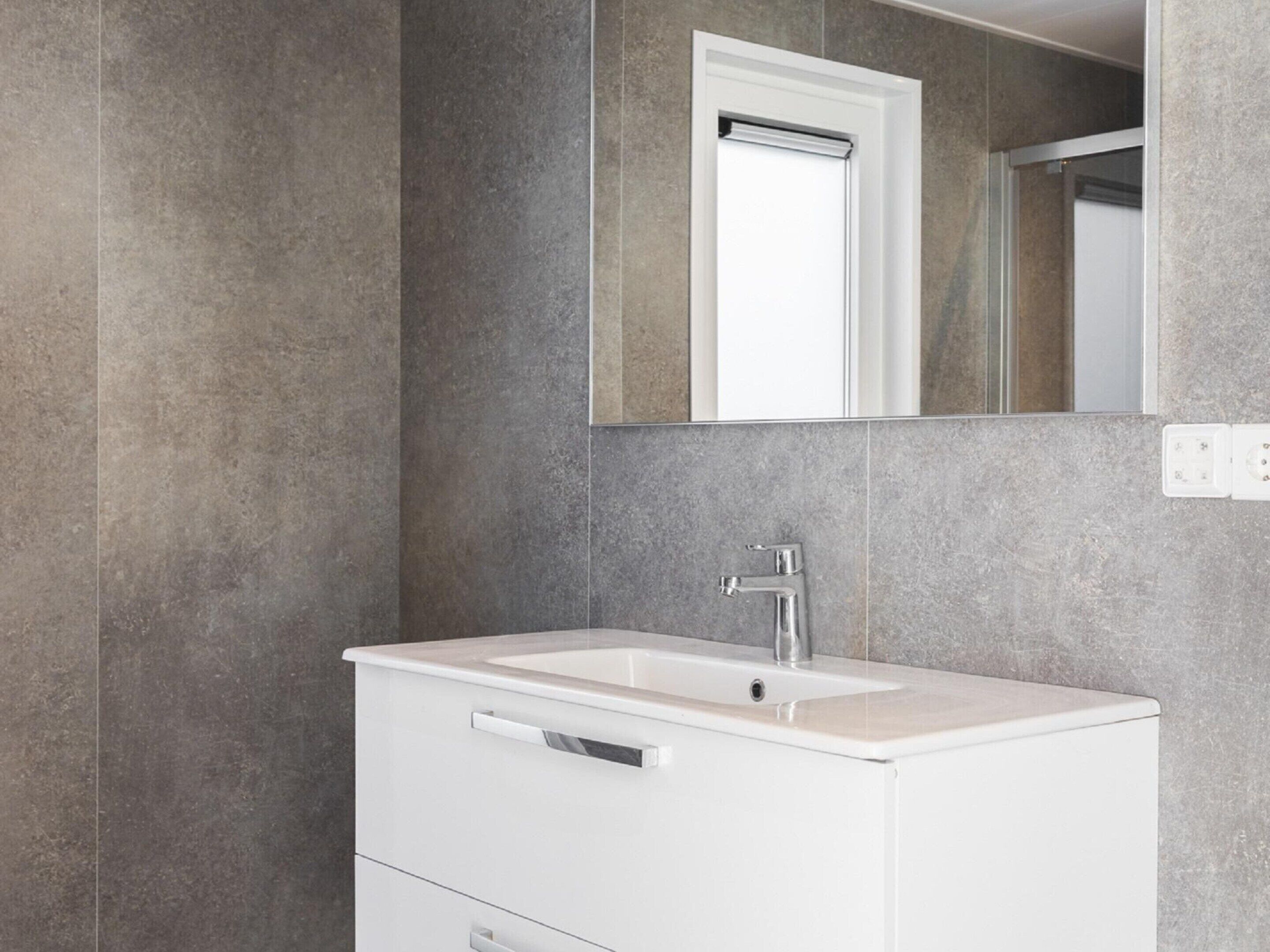 A modern bathroom with a white vanity, a mirror, and a wall-mounted light switch.