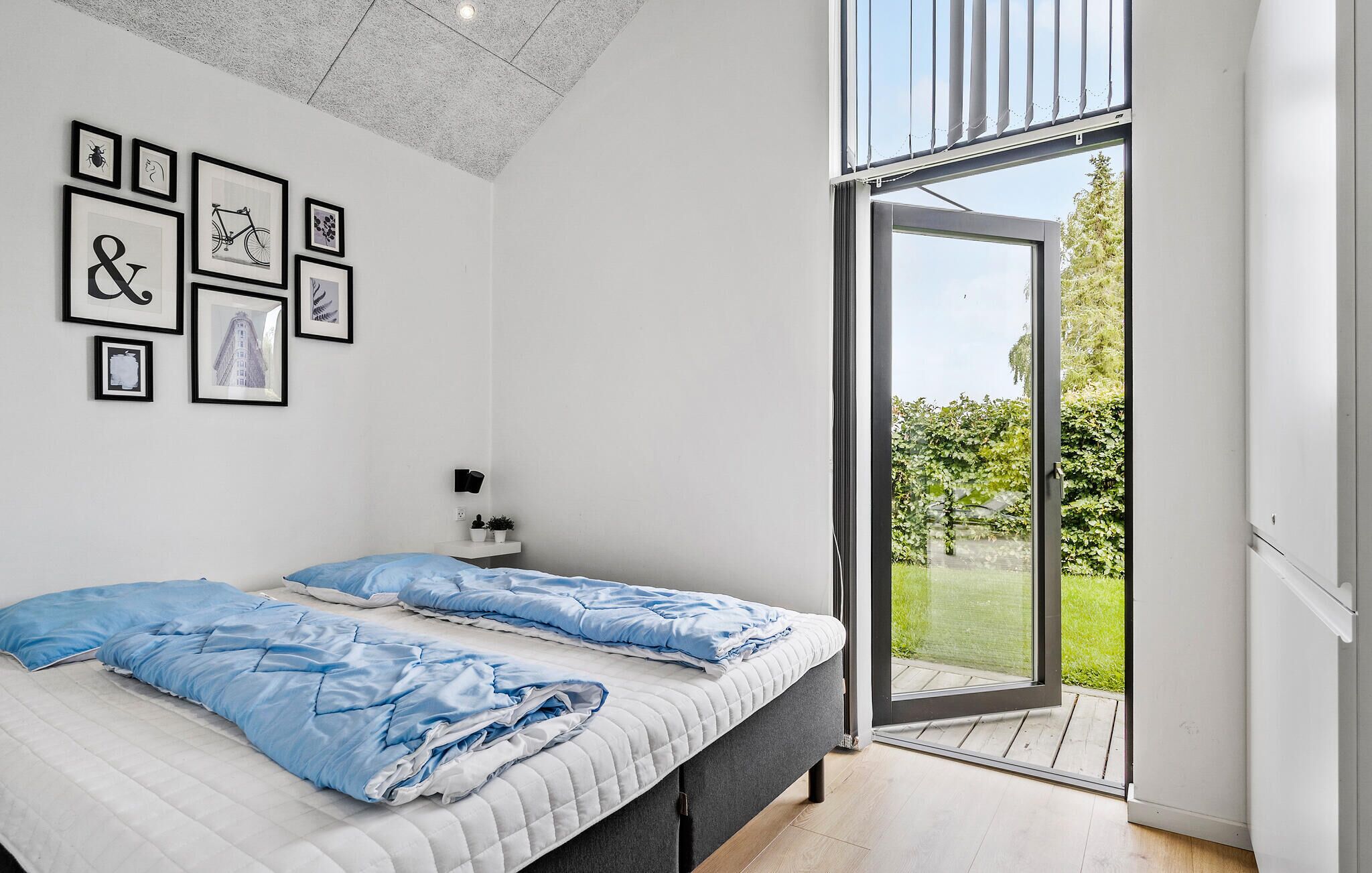 Une chambre à coucher avec un lit, une lampe fixée au mur et une fenêtre donnant sur un paysage verdoyant.