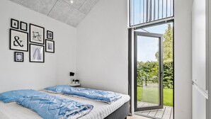 A bedroom with a bed, a wall-mounted light, and a window with a view of greenery.