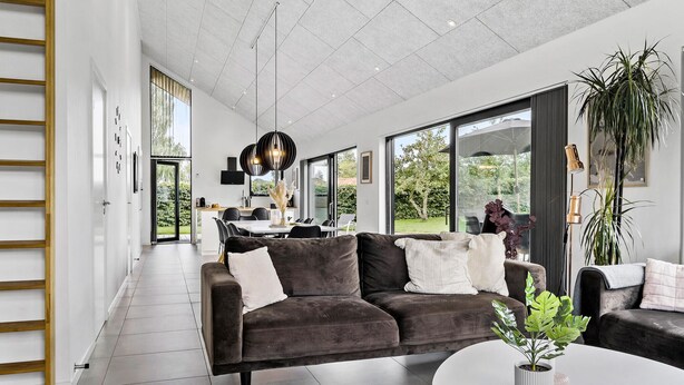 A modern living room with a dark grey sofa, a round coffee table, and a large window offering a view of the outdoors.