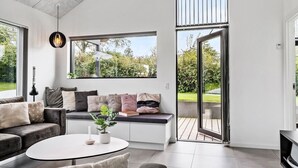 A modern living room with a sofa, a round coffee table, and a large window with a view of a garden.