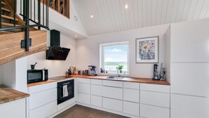 Una cucina moderna con mobili bianchi, un piano di lavoro in legno, un forno a microonde integrato e una finestra con vista sull'esterno.