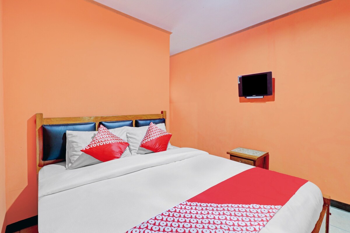 A hotel room with a bed, a nightstand, and a television mounted on the wall.