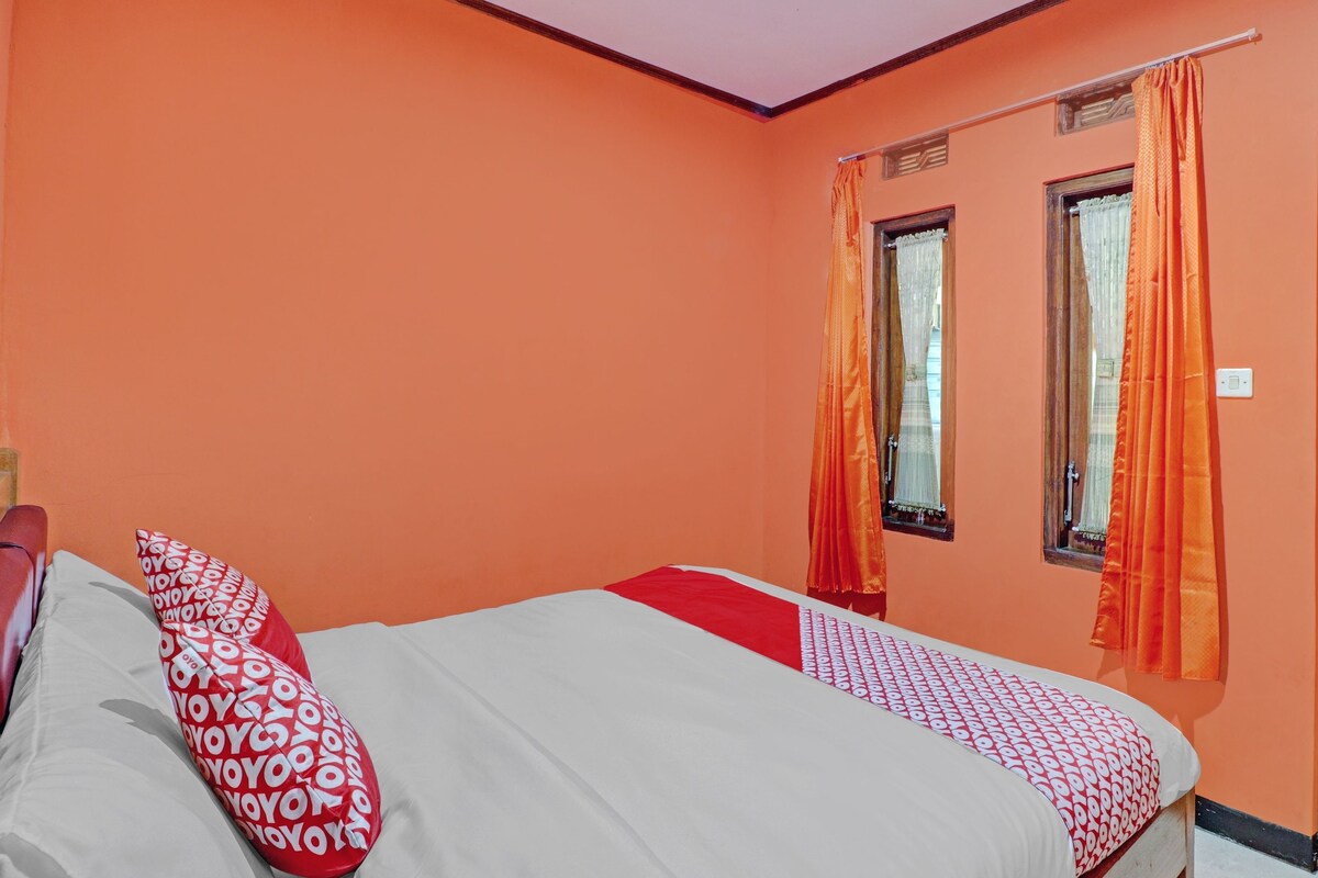 Una habitación con una cama, paredes anaranjadas y dos ventanas con cortinas.