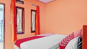 Une chambre à coucher avec un lit, deux fenêtres avec des rideaux et une vue sur l’extérieur.