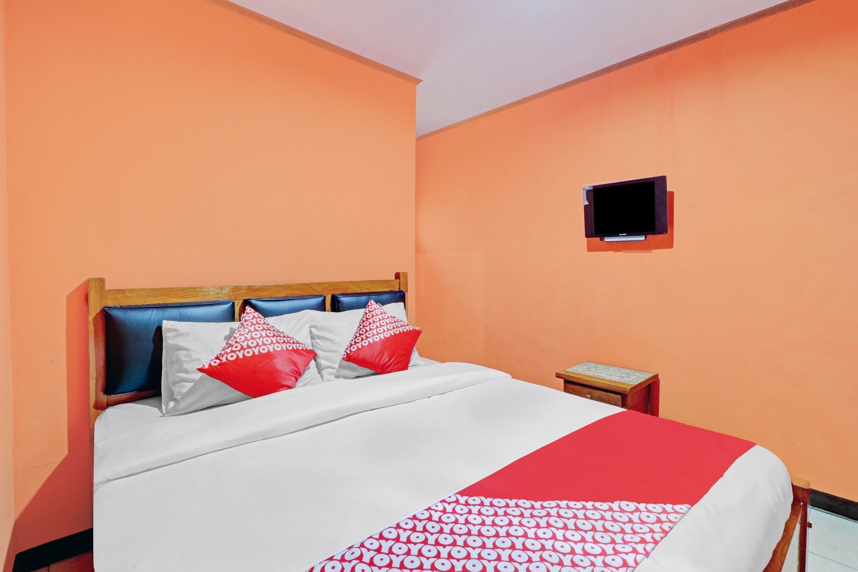 A hotel room with a bed, a nightstand, and a television mounted on the wall.