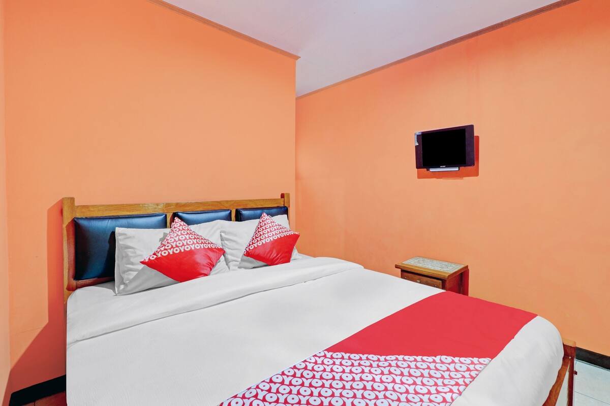 A hotel room with a bed, a nightstand, and a television mounted on the wall.