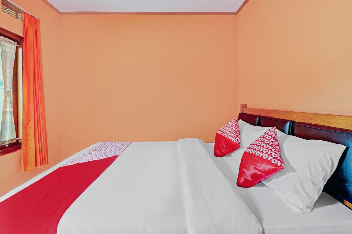 Una cama bien hecha con ropa de cama blanca y roja, un cabecero de madera y una ventana con cortinas naranjas.