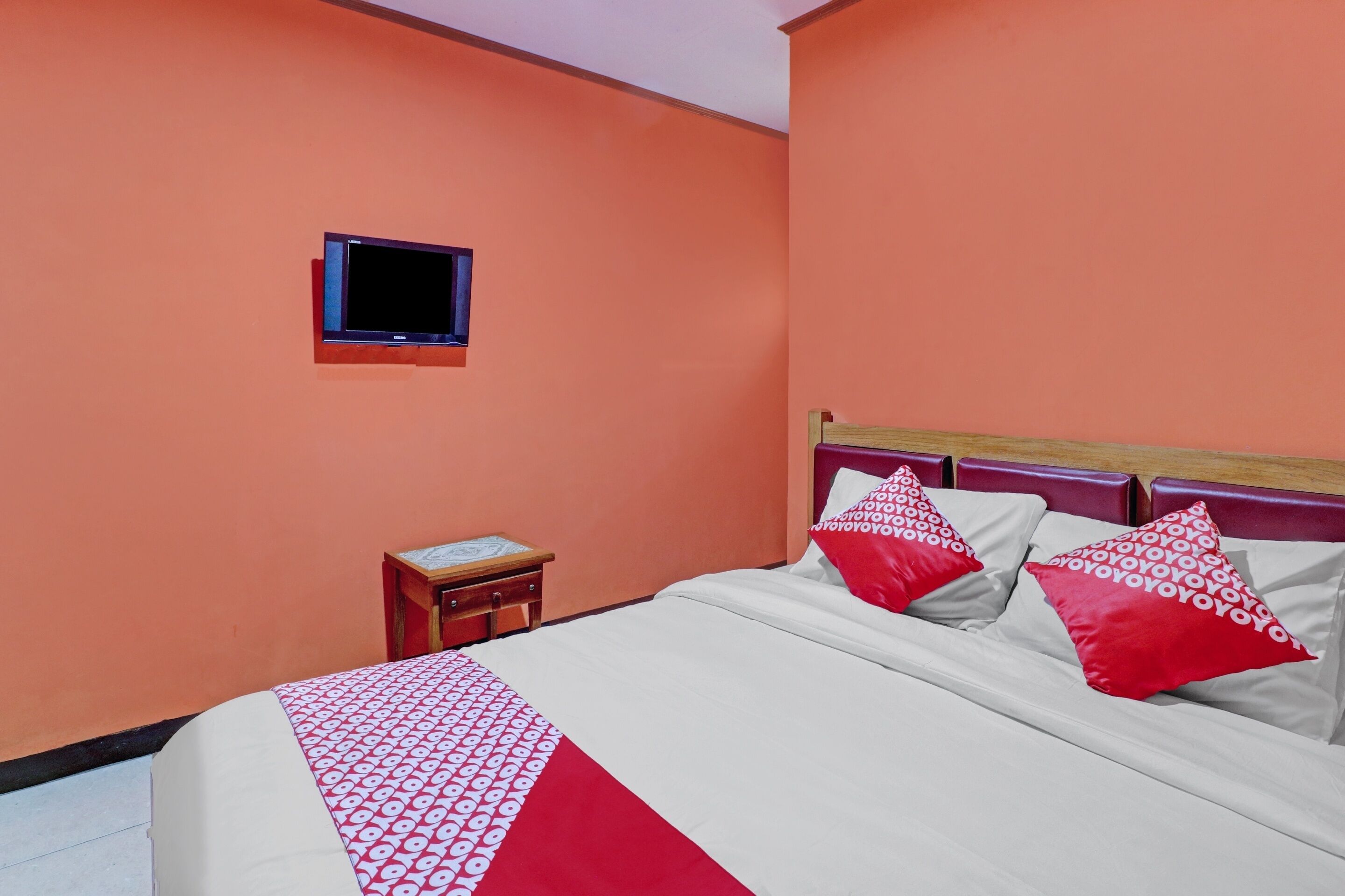 A hotel room with a bed, a small bedside table, a television, and a window.