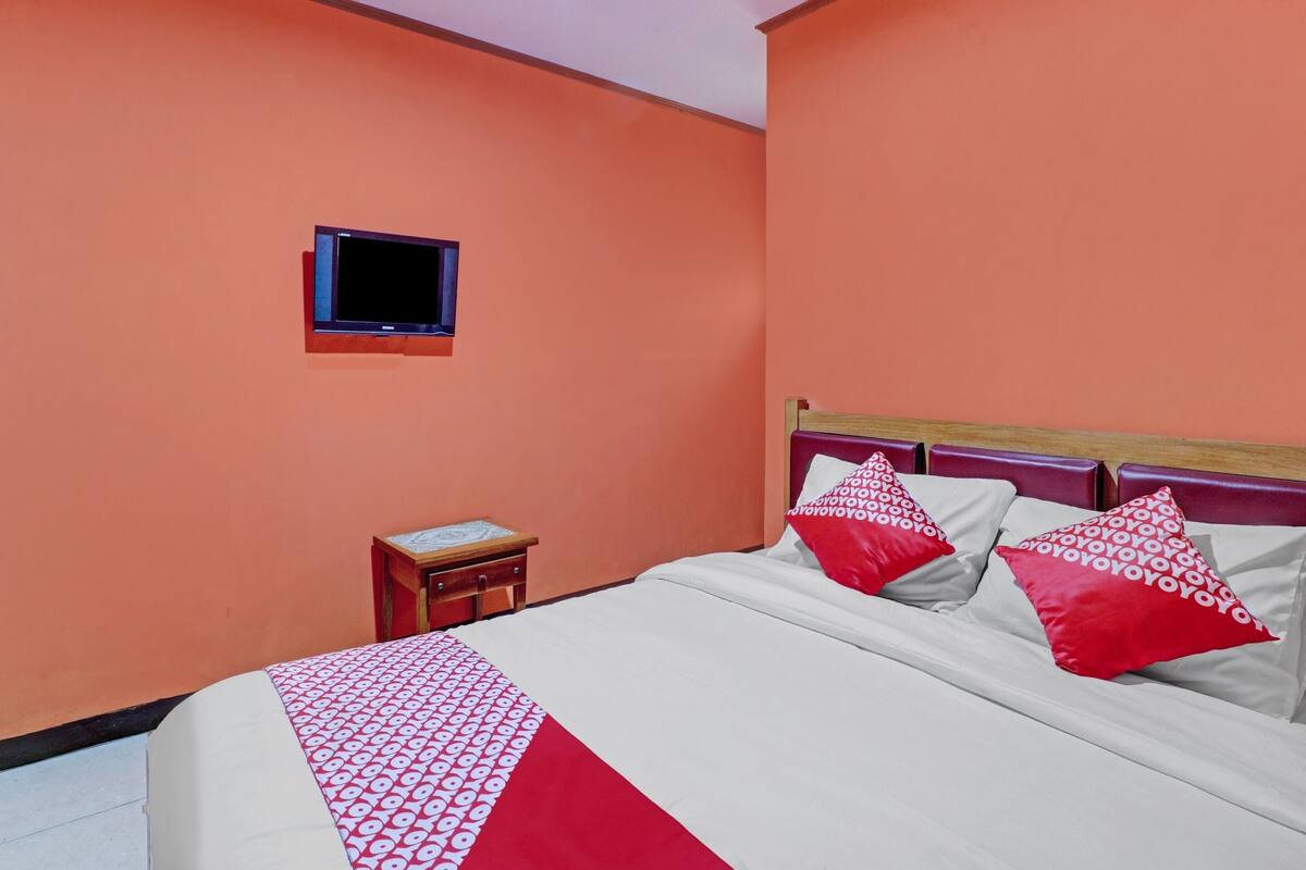 A hotel room with a bed, a small bedside table, a television, and a window.