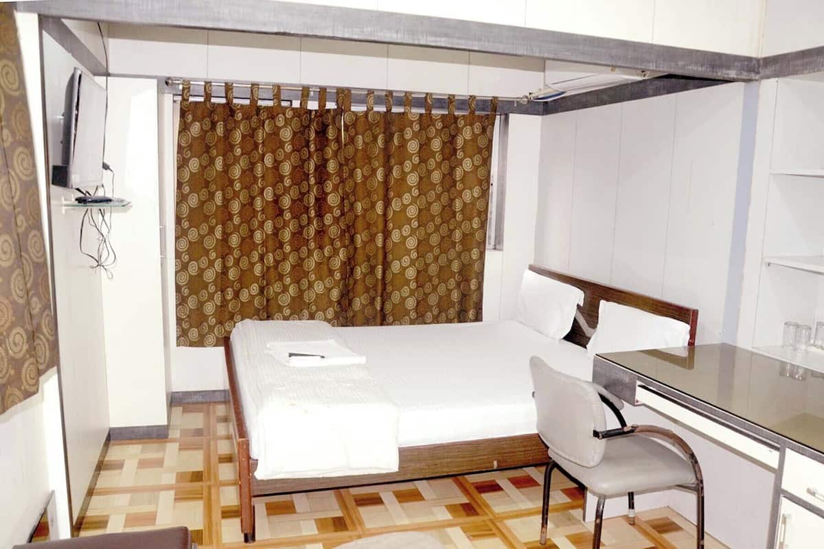 A small, compact hotel room with a single bed, a desk, and a chair.
