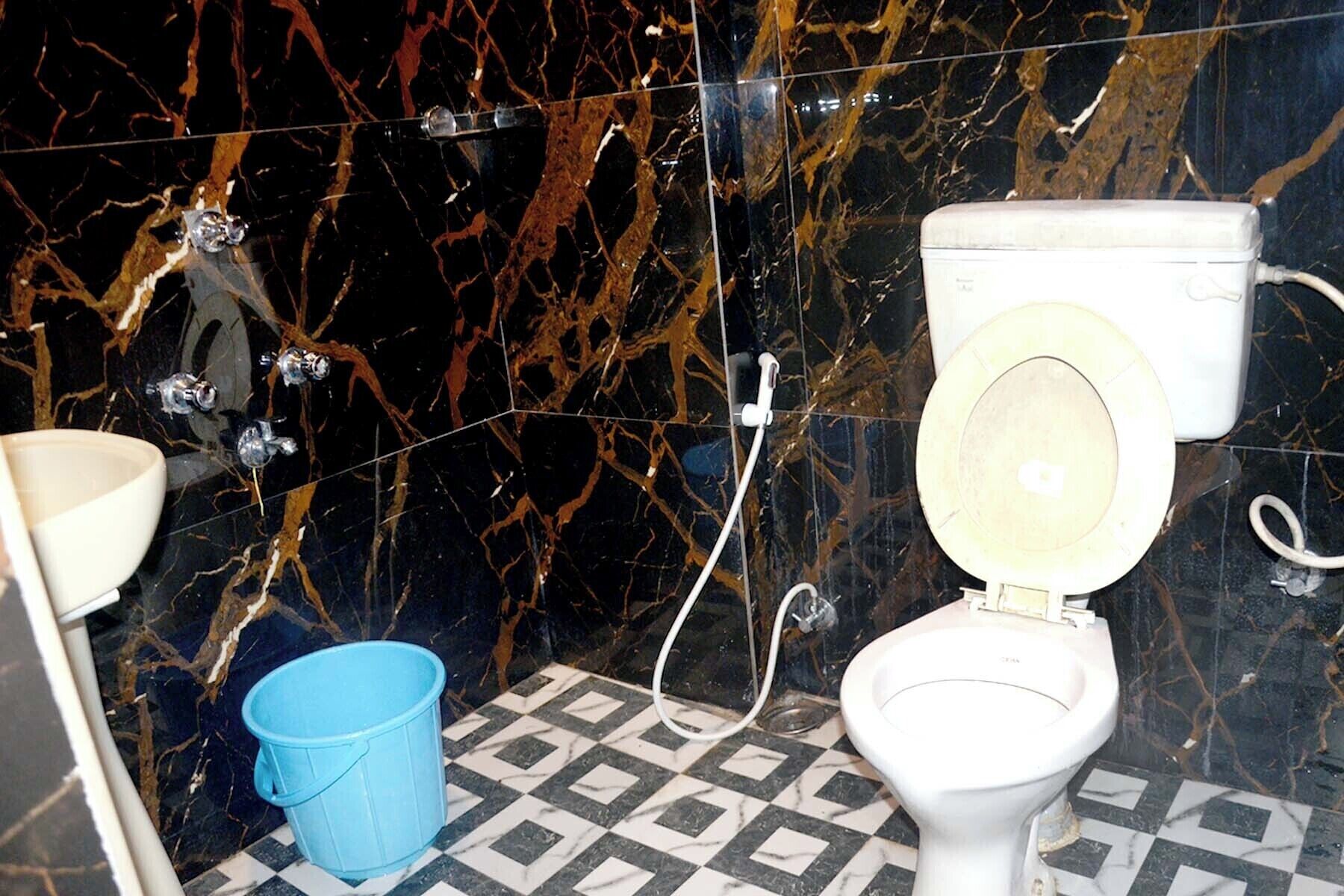 A bathroom with a toilet, a blue bucket, and a marble wall.