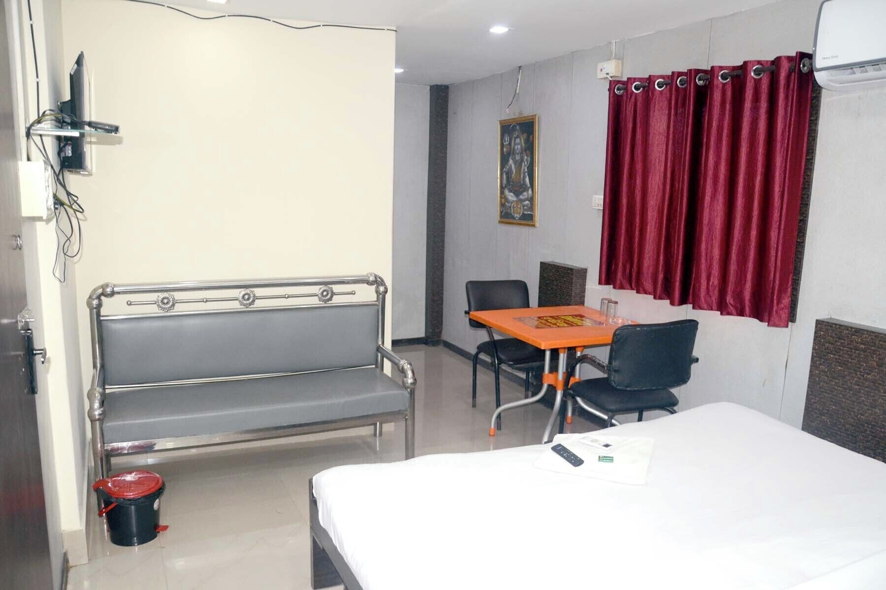 Une chambre d’hôtel avec un lit, une petite table, une chaise, un banc et un rideau rouge.