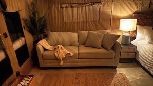 Ein gemütliches Zimmer mit einem beigen Sofa, einem Nachttisch mit Lampe, einer kleinen Pflanze und einer Holzkiste.