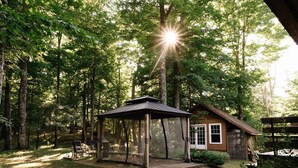 A gazebo with a covered seating area, a wooden cabin, and a forested backdrop. - SPA & Nature | Chalet AYUR (La Minerve)