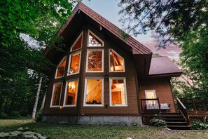 Une cabane en bois à plusieurs étages, dotée d’un toit en pente raide, de grandes fenêtres et d’un escalier apparent menant aux niveaux supérieurs.