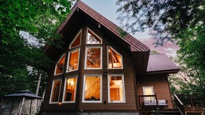 A two-story wooden cabin with multiple windows, a porch, and a staircase leading to the upper level. - SPA & Nature | Chalet AYUR (La Minerve)