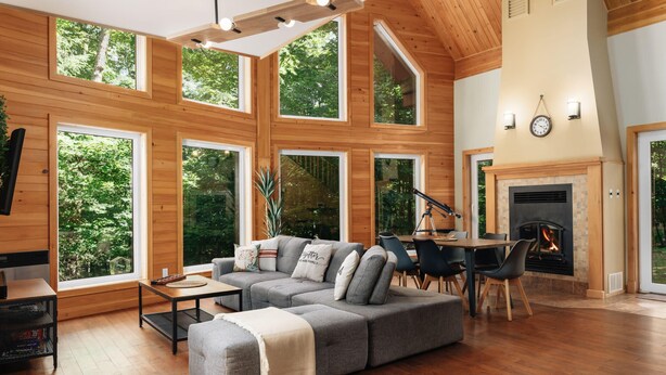 A spacious living room with a large sectional sofa, a fireplace, and large windows offering a view of the outdoors. - SPA & Nature | Chalet AYUR (La Minerve)