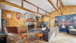 A cozy room with wooden walls, a stone fireplace, a large painting, and a comfortable seating area. - Waterfront - Spa | Havre de l'Auror | Harry Potter (Outaouais)