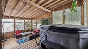 A wooden deck with a hot tub, seating area, and large windows overlooking a snowy landscape. - Waterfront - Spa | Havre de l'Auror | Harry Potter (Outaouais)
