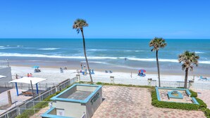 A beach view with palm trees, a sandy beach, and a paved walkway. - Oceanfront 1BR | Amazing Views + Private Balcony (Daytona Beach)
