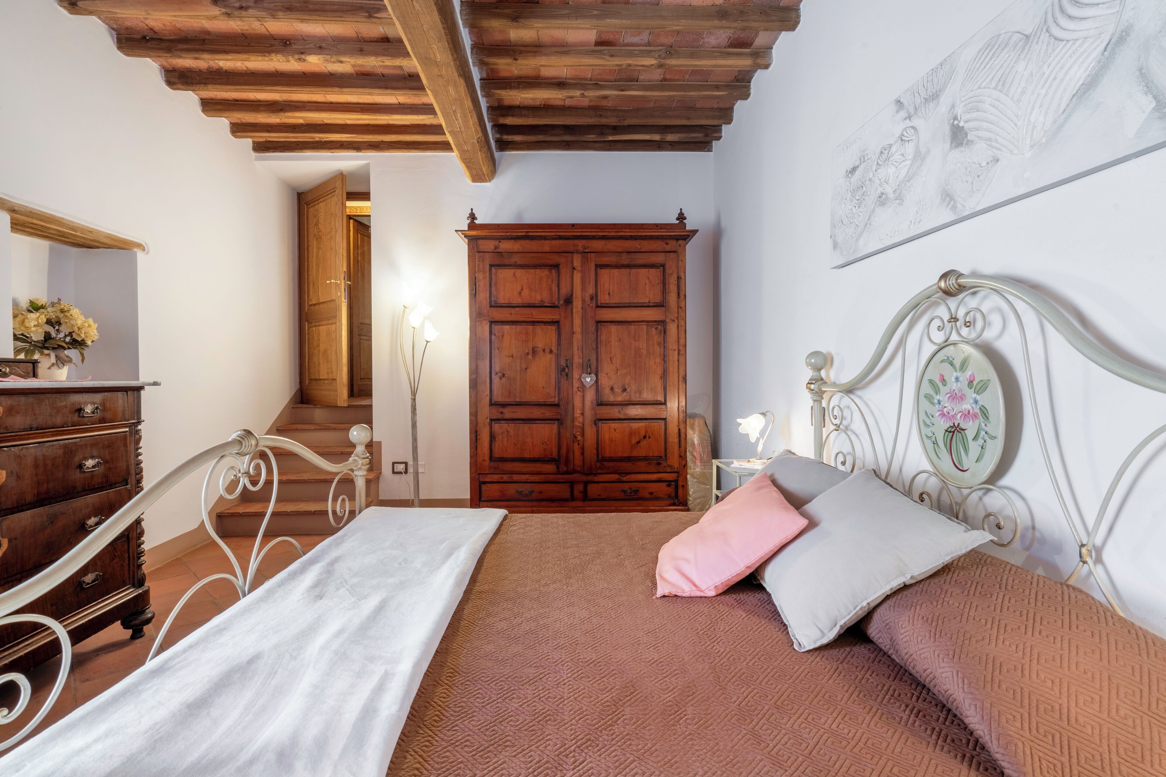 Une chambre à coucher avec un lit, une armoire en bois et un escalier menant à une autre pièce.