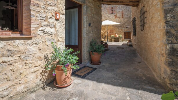 Un bâtiment en pierre avec une porte en bois, des plantes en pot et un sol carrelé.