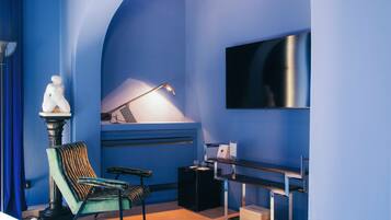 A room with a blue wall, a mounted TV, a desk with a lamp, and a chair.
