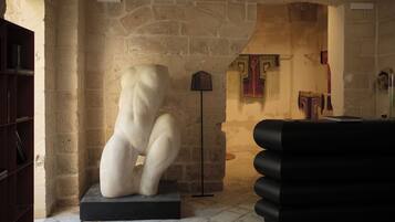 Une pièce aux murs de pierre, avec une sculpture blanche, un lampadaire noir et un canapé noir.