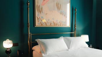 Quarto de hotel com paredes verde-água, cama com roupa de cama branca, quadro emoldurado sobre a cama, abajur e telefone na mesa de cabeceira.