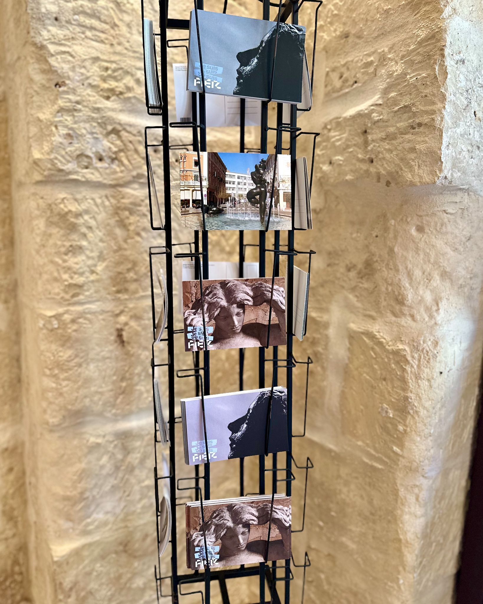 A vertical display of postcards on a metal rack against a textured wall.