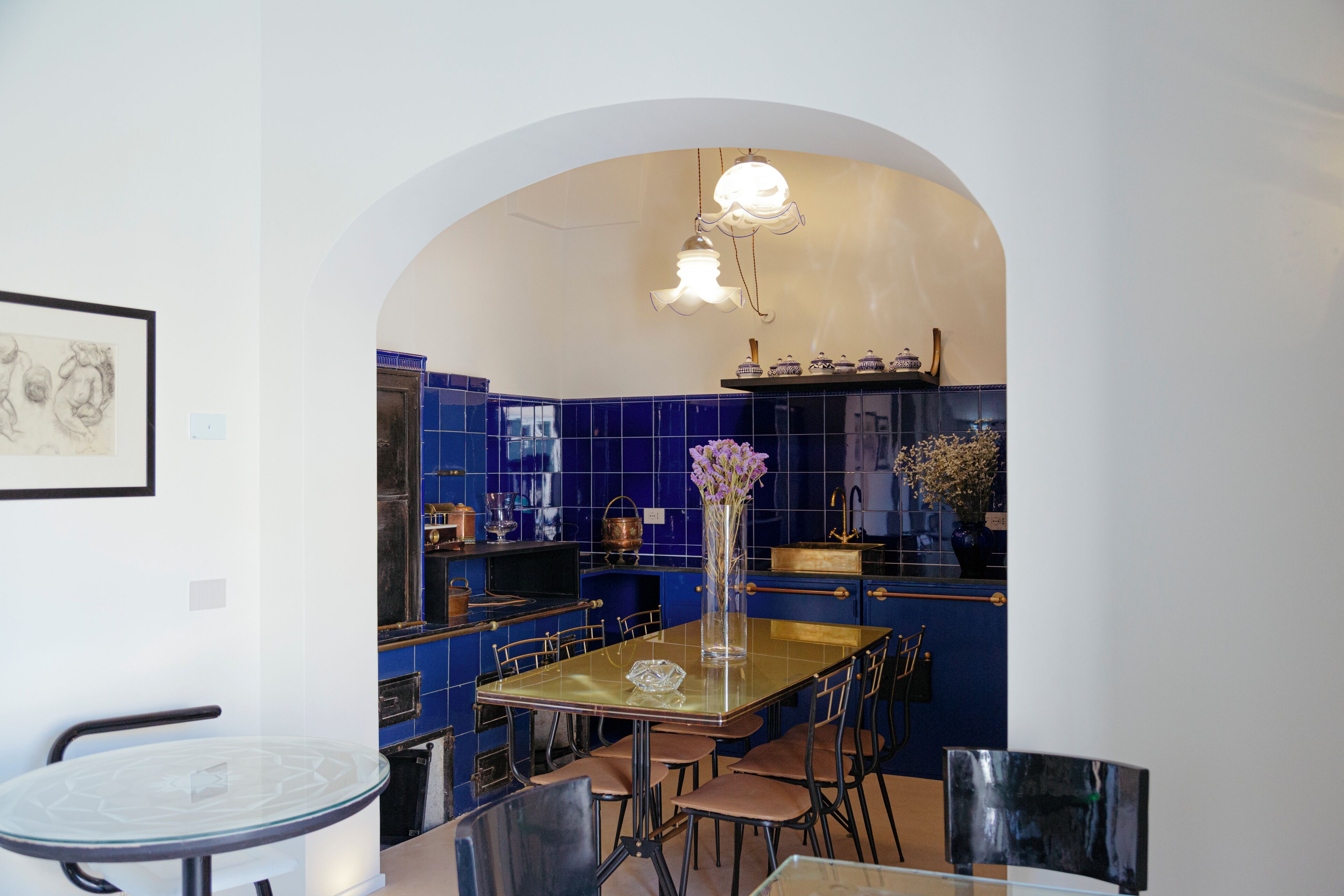 Une cuisine moderne avec une table à manger en verre, des carreaux bleus et un vase rempli de fleurs.