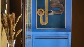A hallway with a blue wall, a large abstract artwork, a glass door, and a vase with dried plants.