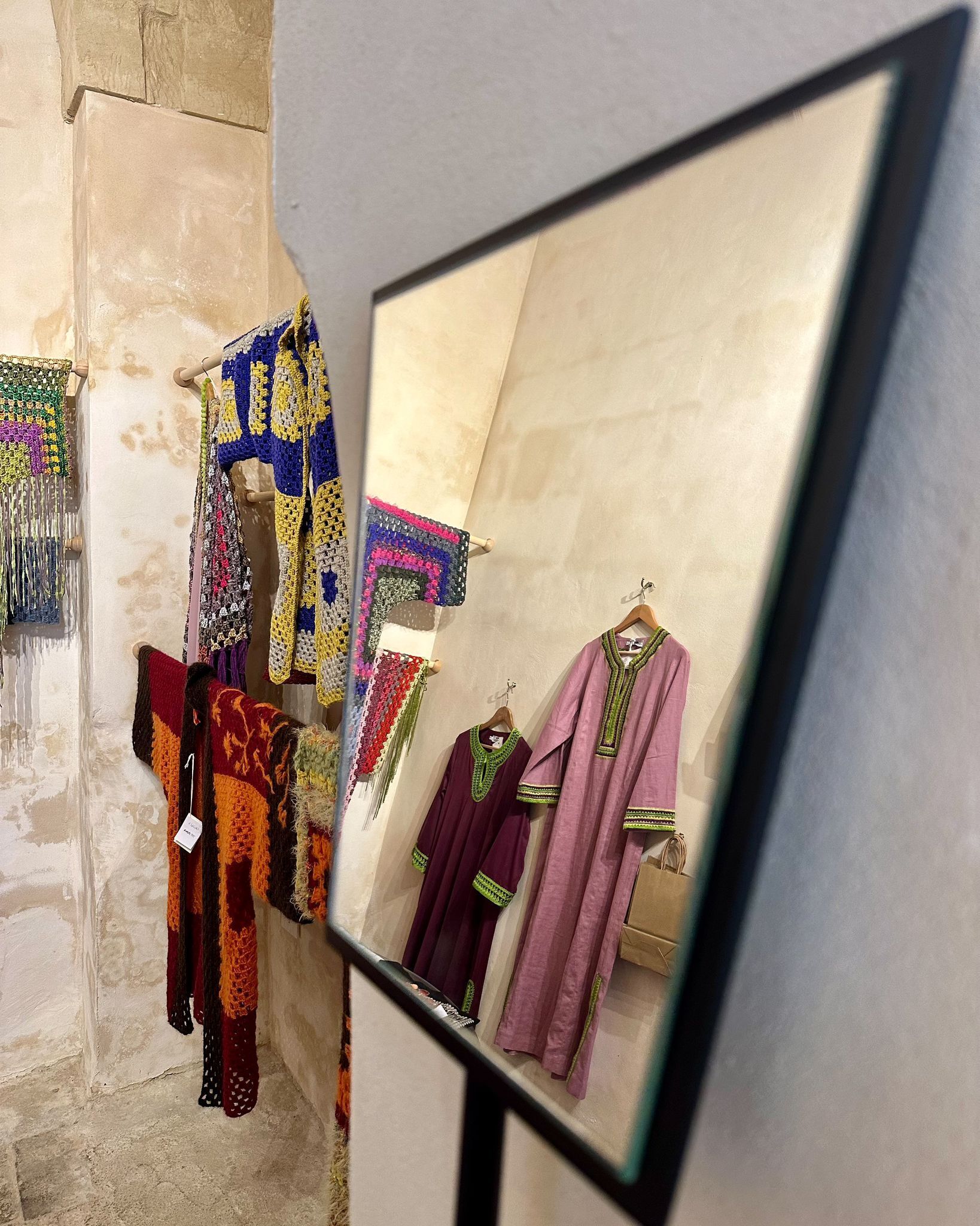 A display of colorful garments and accessories, including a maroon dress with green trim and a pink dress with green trim, both hanging on hangers.