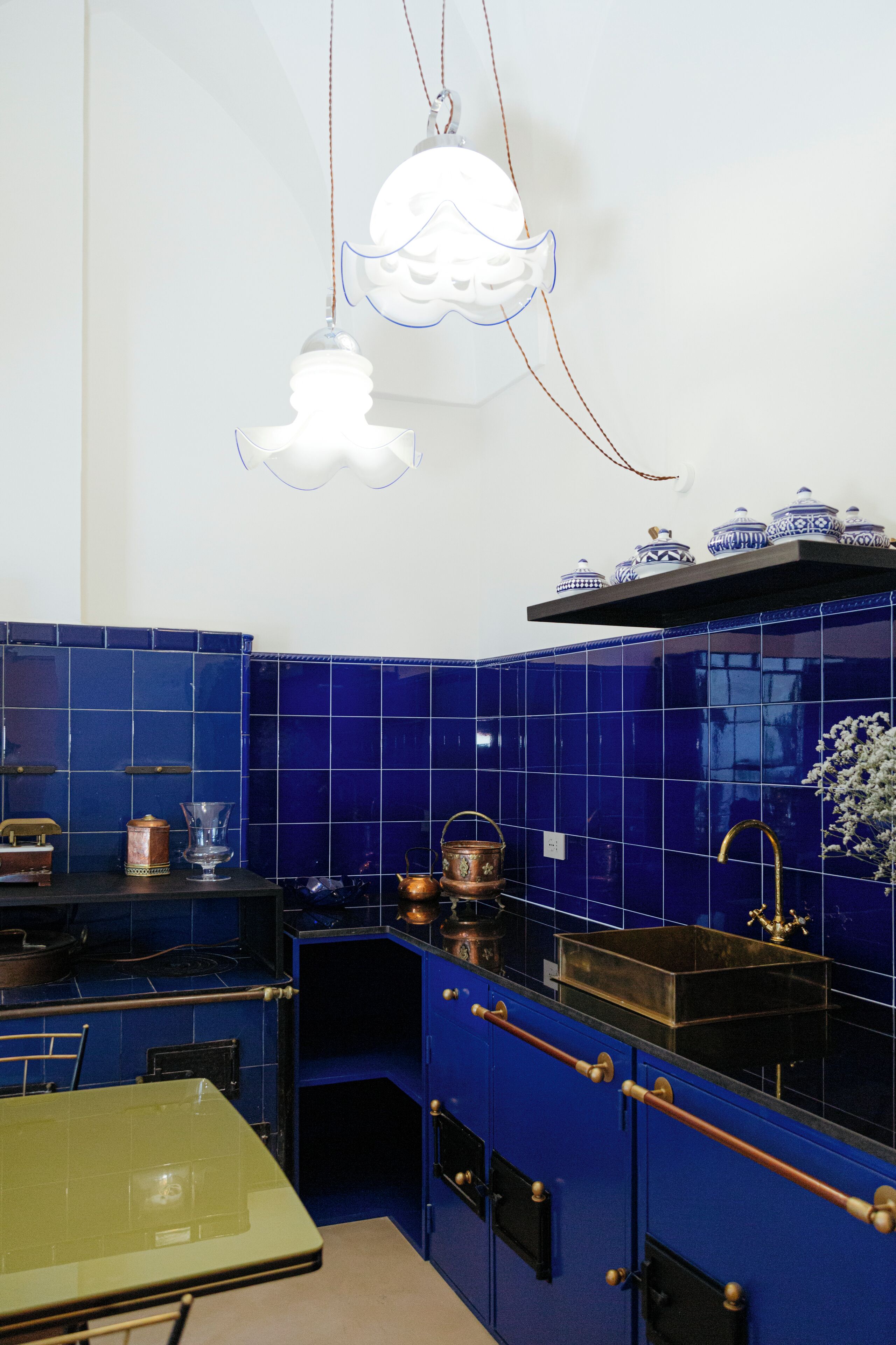 A kitchen with blue tiles, a black countertop, and a white hanging light fixture.
