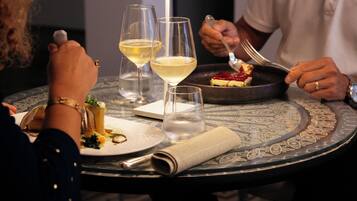 Una mesa redonda con mantel estampado, dos copas de vino, un vaso de agua y un plato de postre con un tenedor.