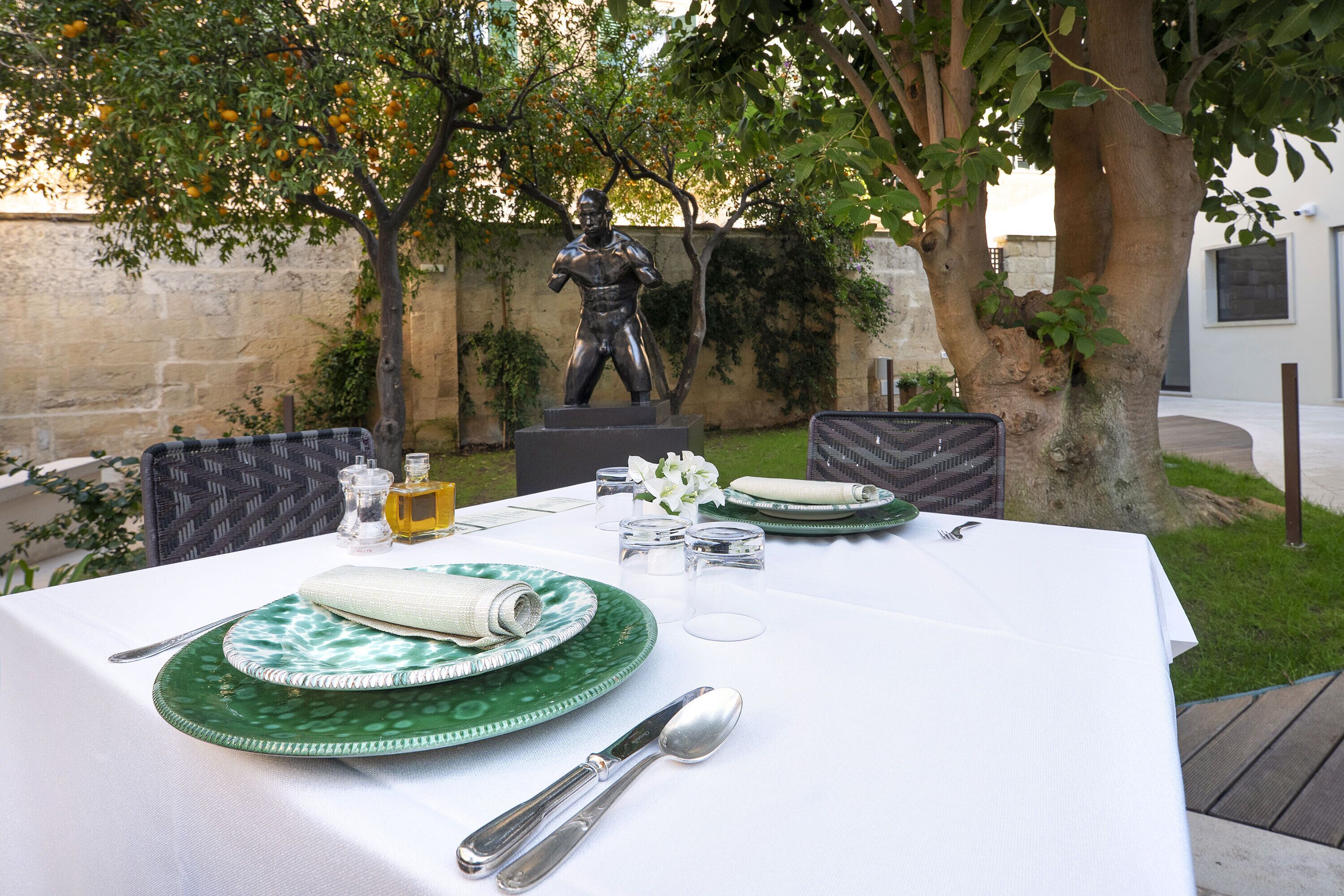 An outdoor dining table set with green plates, silverware, and a statue in the background.