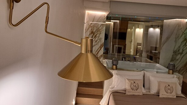 A modern bathroom with a gold-colored wall-mounted lamp, a large mirror, and a marble-topped sink. - Elegant Suite in the heart of Naples  (Napoli)