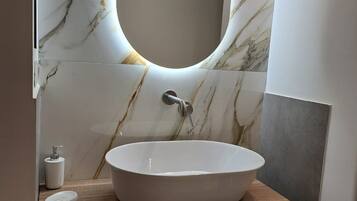 Une salle de bain avec un pare-baignoire en marbre, un lavabo sur pied, un miroir et un porte-serviettes avec des serviettes.