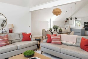 A modern living room with a grey sofa set, a coffee table, and a dining area in the background. - Hill View House - Cookswood, Somerset | Hot Tub | Sleeps 8 (Somerset)