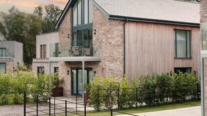 A modern two-story house with stone and wood exterior, large windows, and a balcony. - Hill View House - Cookswood, Somerset | Hot Tub | Sleeps 8 (Somerset)