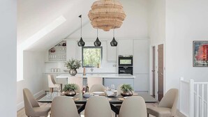 A modern kitchen with a dining area, featuring a large island, pendant lights, and a view of the outdoors. - Hill View House - Cookswood, Somerset | Hot Tub | Sleeps 8 (Somerset)