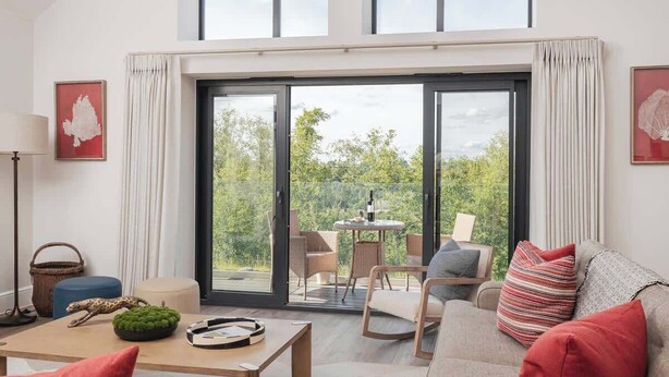 A modern living room with a sofa, a coffee table, and a dining area with chairs and a table. - Hill View House - Cookswood, Somerset | Hot Tub | Sleeps 8 (Somerset)