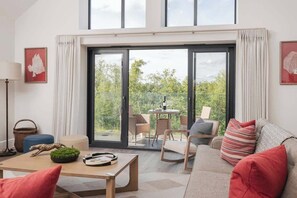 A modern living room with a sofa, a coffee table, and a dining area with chairs and a table. - Hill View House - Cookswood, Somerset | Hot Tub | Sleeps 8 (Somerset)