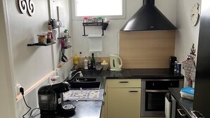 Eine kompakte Küche mit einer schwarzen Dunstabzugshaube, einem Einbauofen, einem Spülbecken und einem Fenster über der Arbeitsfläche.